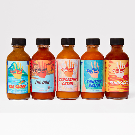 Five small glass bottles of Culture Hot Sauce lined up against a clean white background. The bottles contain orange-red sauce and feature colorful labels with tropical designs and names including Bar Sauce, The Don, Tangerine Dream, Tahitian Dream, and Blindsided.