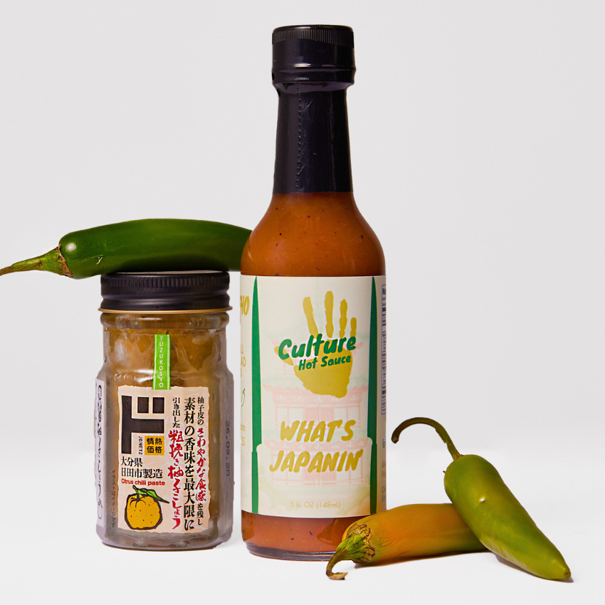 A bottle of Culture Hot Sauce 'What's Japanin'' and a jar of Japanese Yuzu Kosho with green chili peppers on a light gray background.